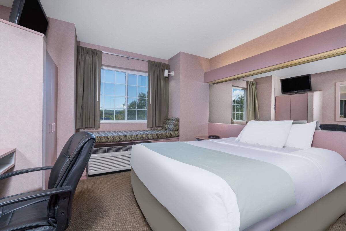 Een hotelkamer met een bed, een televisie, een bureau en een raam met gordijnen.