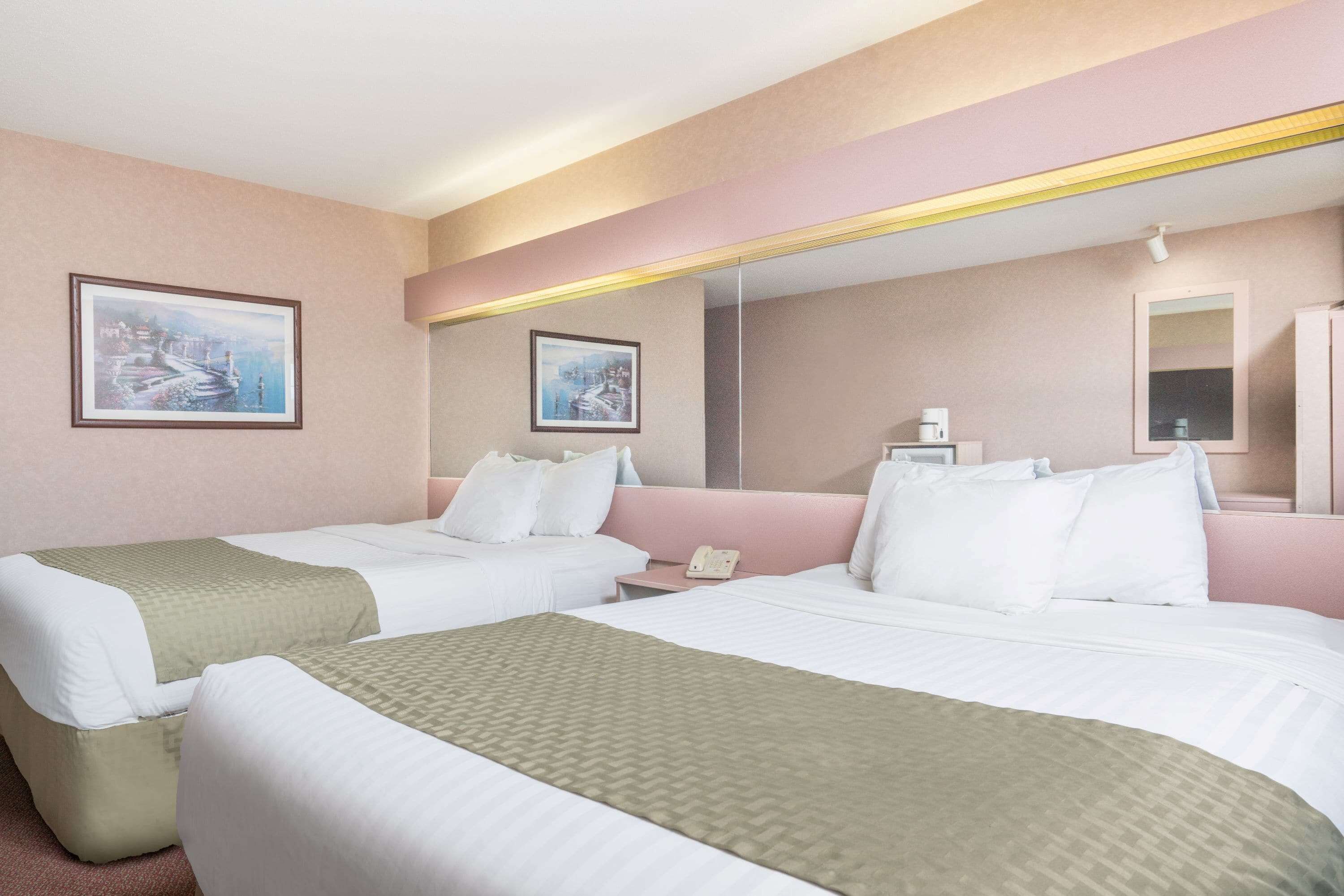 A hotel room with two beds, a bedside table with a phone, and artwork on the walls.