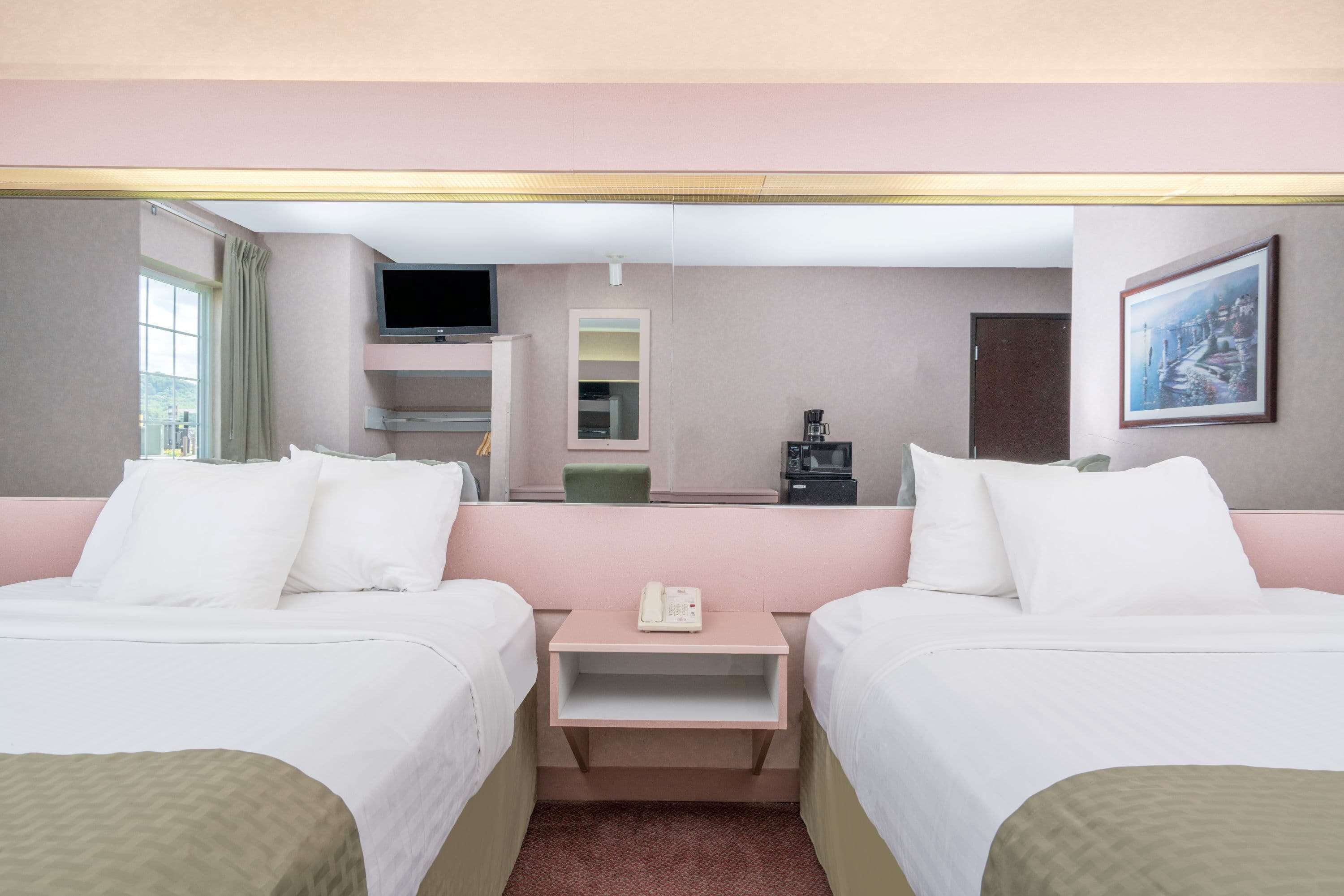 Habitación de hotel con dos camas, una mesita con un teléfono, televisión, cafetera y un cuadro en la pared.