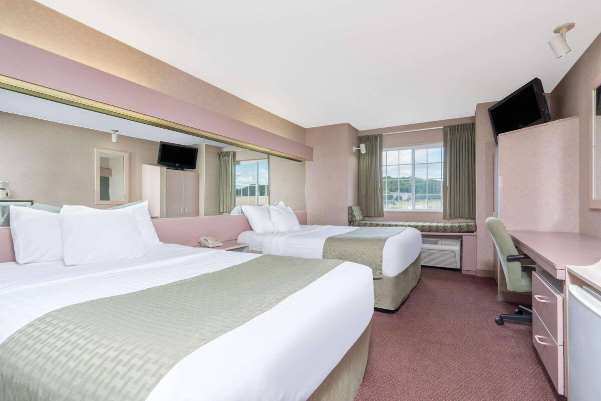 Een hotelkamer met twee bedden, een bureau, een stoel, een televisie en een raam met uitzicht.