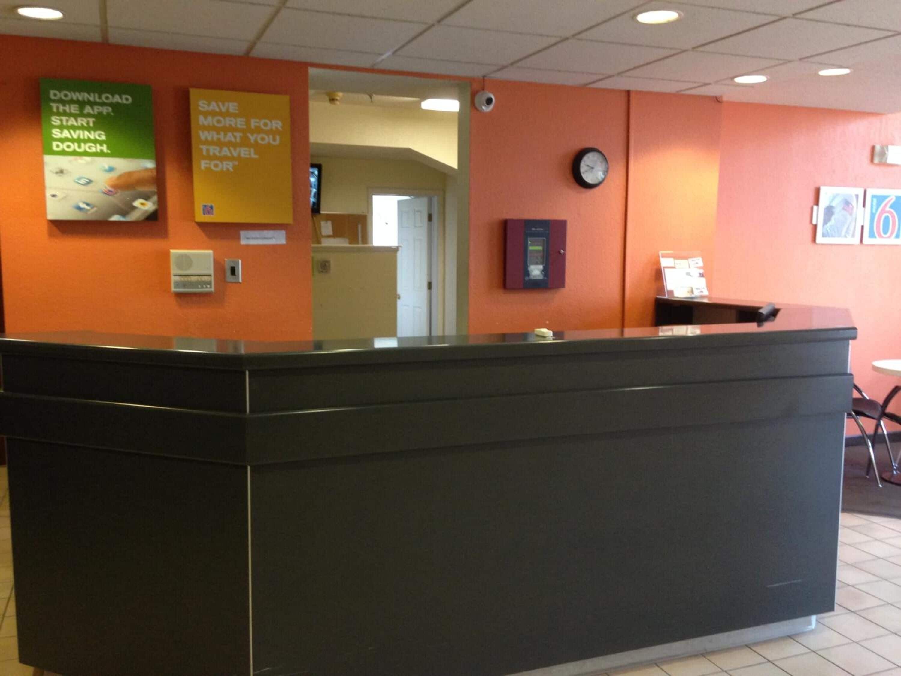 A reception area with a black counter, orange walls, a clock, and two posters advertising travel savings and a mobile app.
