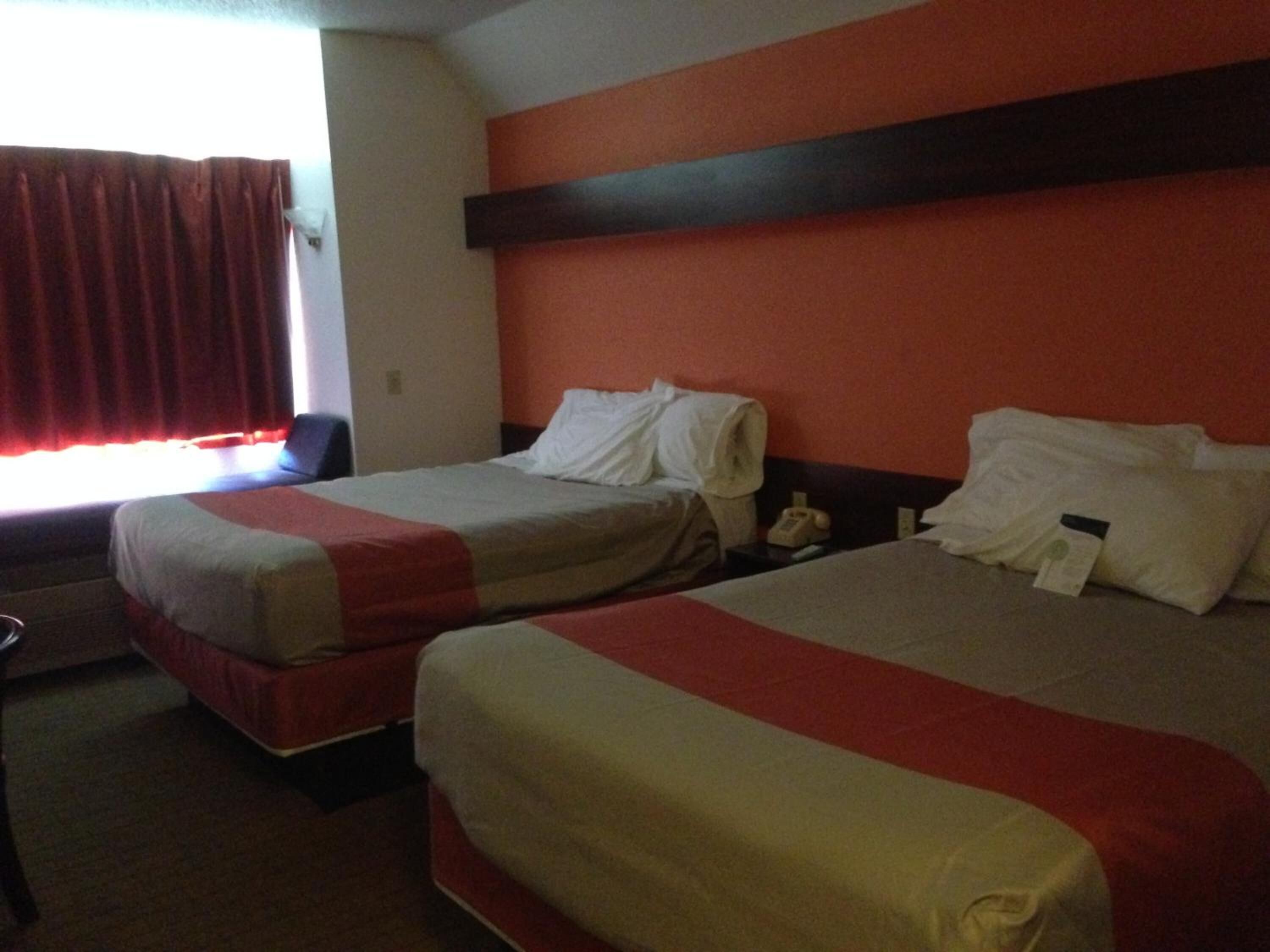 A hotel room with two beds, a red and white color scheme, and a window with red curtains.