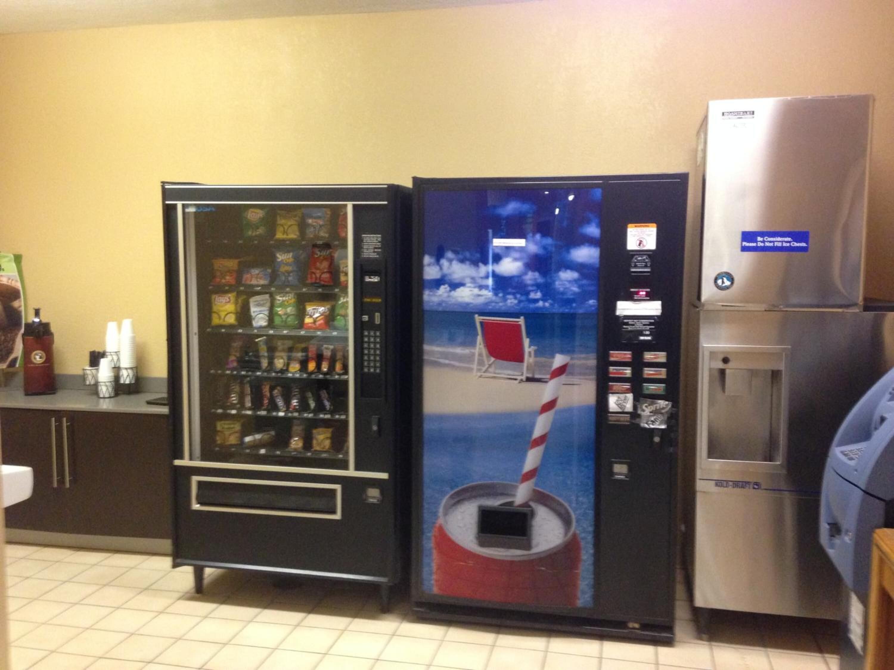 A vending machine with snacks and a drink dispenser, a refrigerator, and a water cooler in a commercial setting.