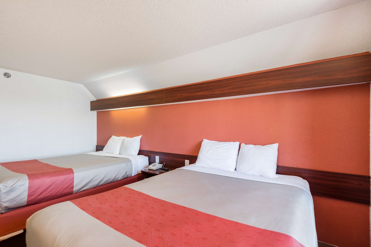 A hotel room with two beds, each with white bedding and a red accent.