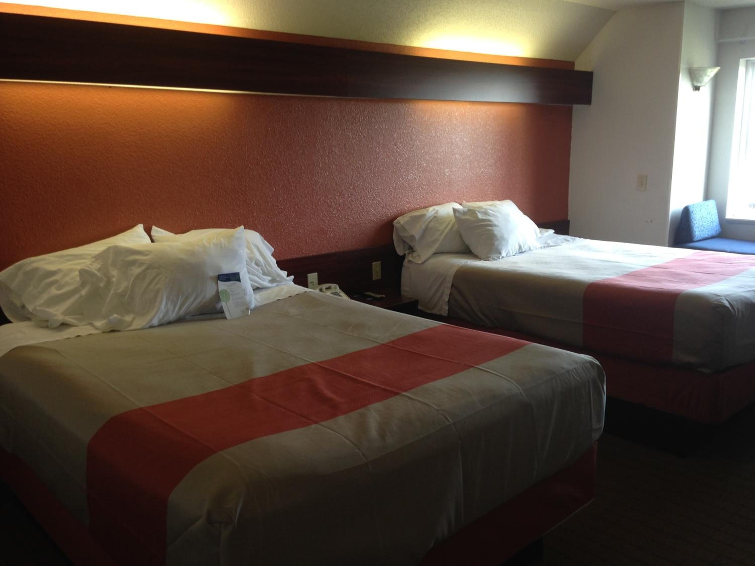 Two single beds with white linens and red accents, a wooden headboard, and a window with daylight.
