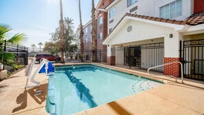 Una piscina con una silla azul, una escalera metálica y una entrada con portón.