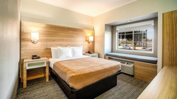 Una habitación de hotel con cama, mesitas de noche, ventana con vistas y un banco empotrado.
