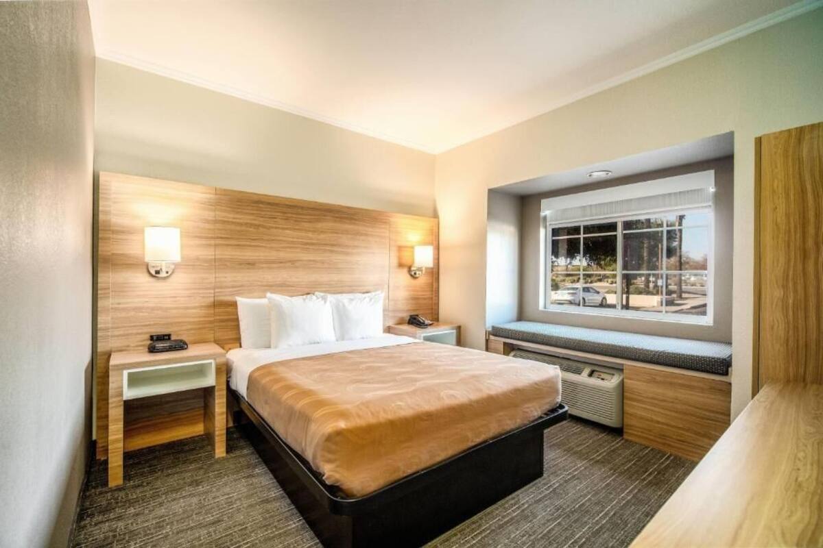 Una habitación de hotel con cama, mesitas de noche, ventana con vistas y un banco empotrado.