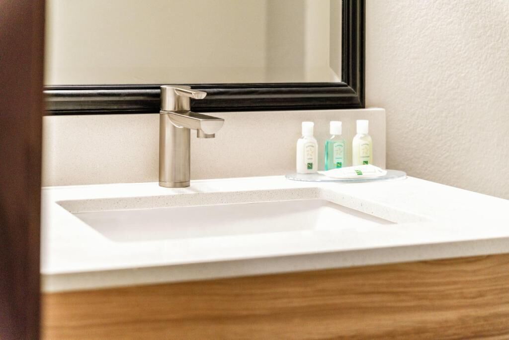 Ein Badezimmer mit einem weißen Waschbecken, einem Spiegel und drei Kosmetikprodukten auf der Ablagefläche.