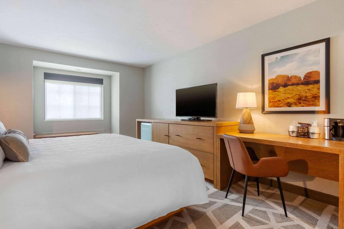 A hotel room with a bed, a desk, a television, a lamp, and a painting on the wall.