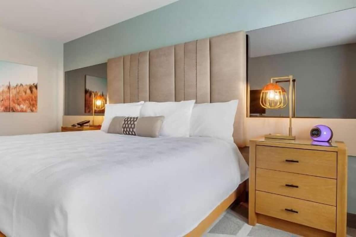 A neatly made bed with a headboard, a bedside table with drawers, and a wall-mounted lamp.