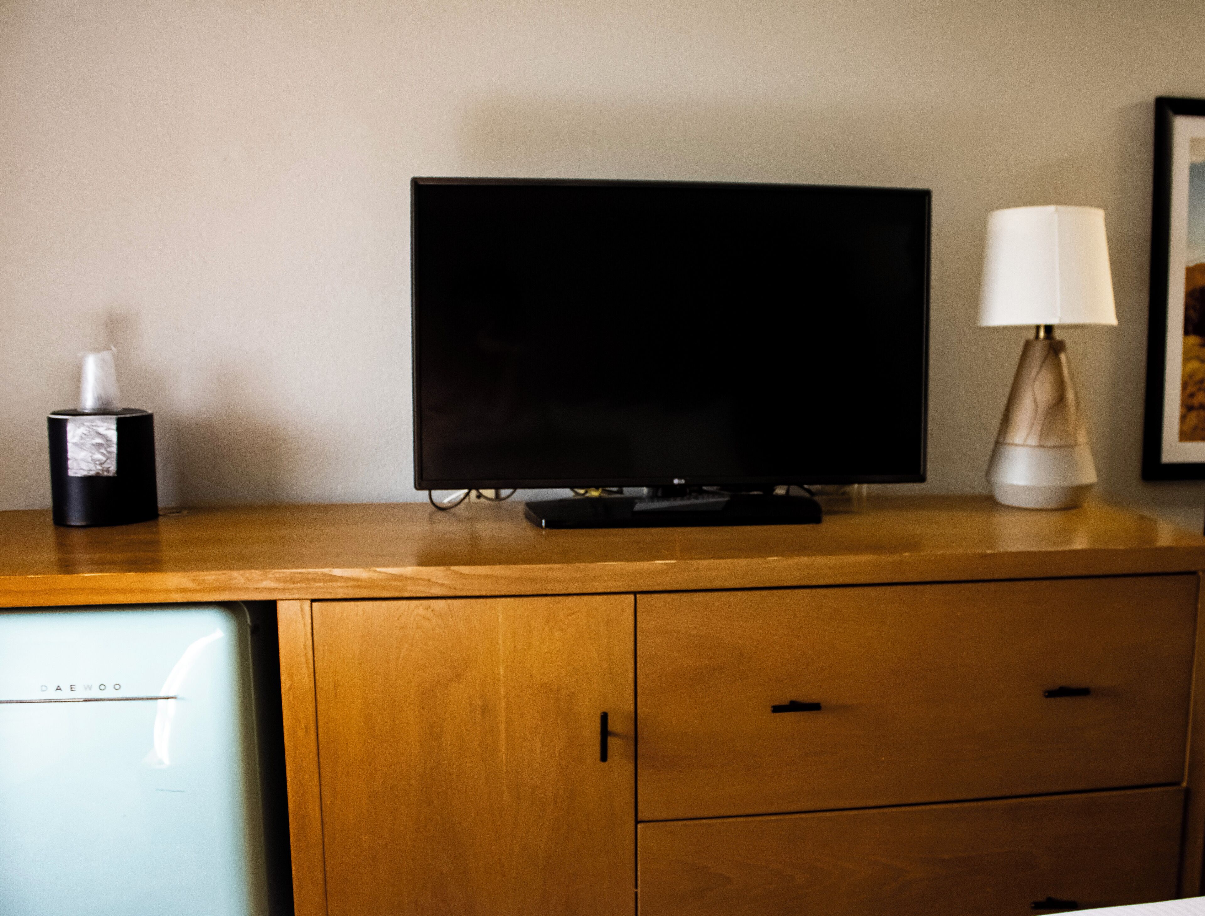 Een houten tv-meubel met een flatscreen televisie, een zakdoos en een lamp.