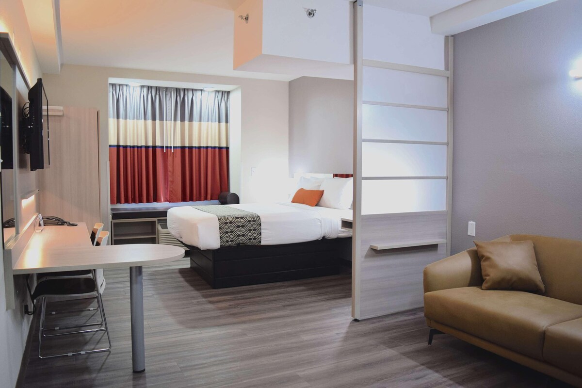 Une chambre d’hôtel avec un lit, un bureau, un canapé et une fenêtre avec des rideaux.