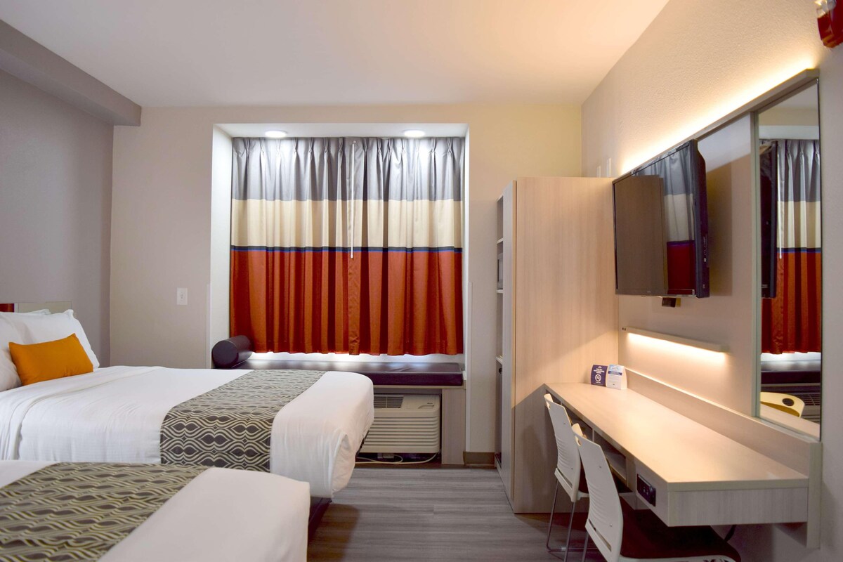 Une chambre d’hôtel avec deux lits, un bureau, une télévision et une fenêtre avec des rideaux.