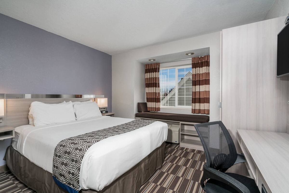 Une chambre d’hôtel avec un grand lit, un bureau, une chaise, une télévision et une fenêtre avec des rideaux.