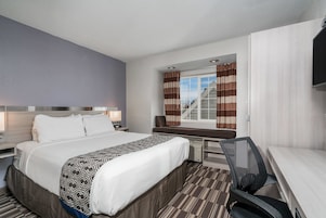 Habitación de hotel con una cama grande, un escritorio, una silla, un televisor y una ventana con cortinas.