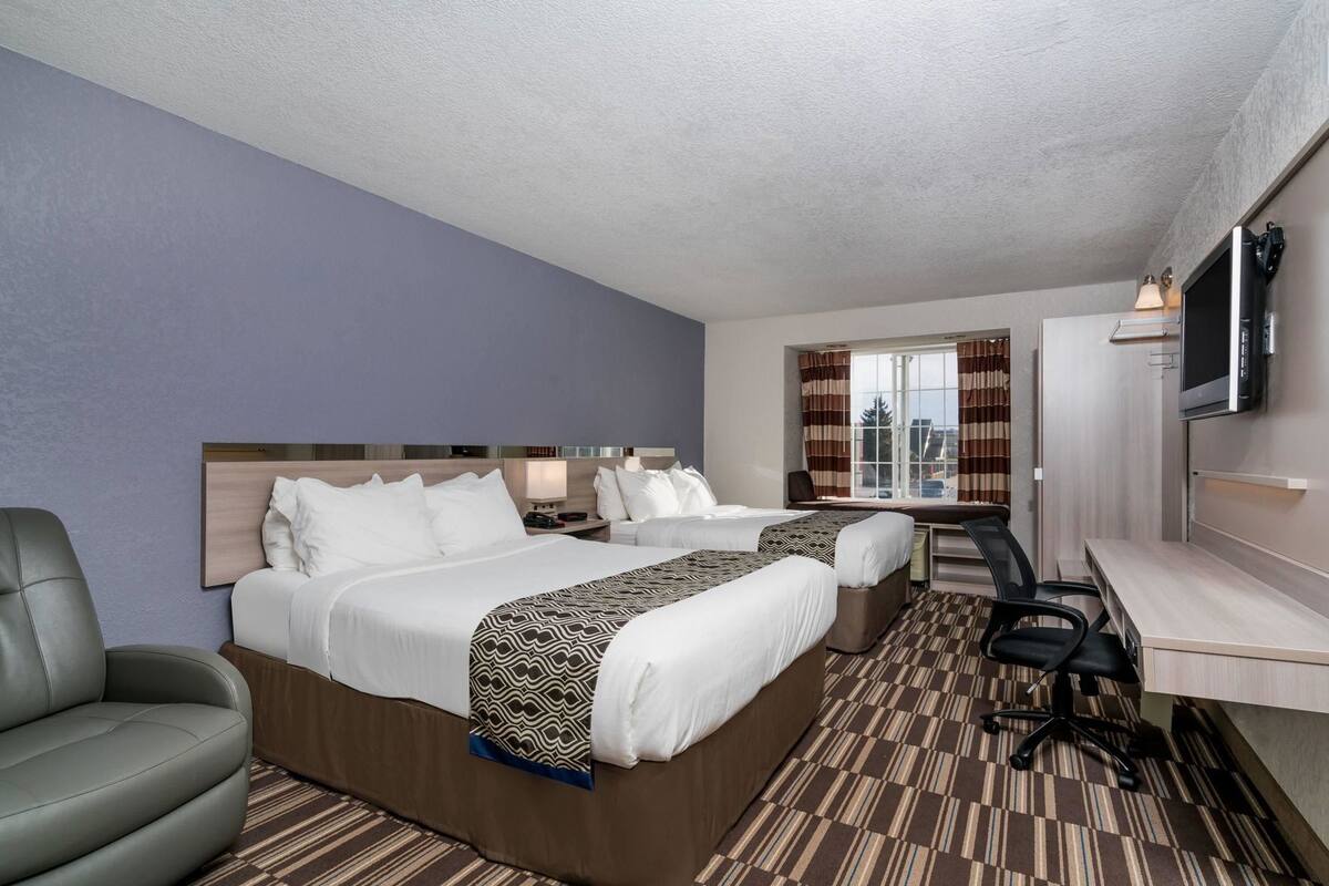 Une chambre d’hôtel avec deux lits, un bureau, une chaise, une télévision et une fenêtre avec des rideaux.