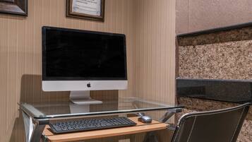 A hotel room with a glass desk, a computer monitor, keyboard, and mouse.