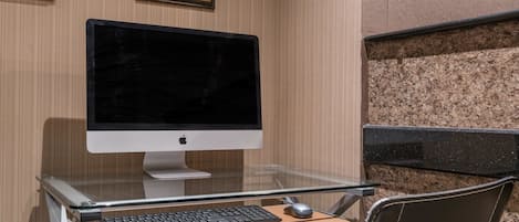 Una habitación de hotel con un escritorio de cristal, un monitor de computadora, teclado y ratón.