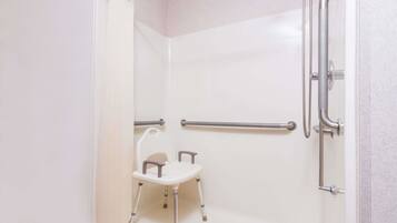 A shower area with a white bathtub, grab bars, and a small white chair.