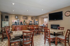 A restaurant with wooden chairs and tables, a counter with a coffee machine, and a television on the wall. - Microtel Inn & Suites by Wyndham Rochester North Mayo Clinic (Rochester)