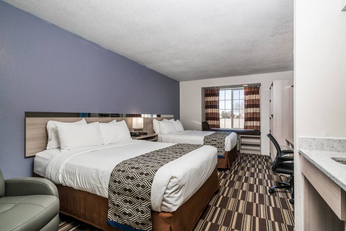 Une chambre d’hôtel avec deux lits, un bureau, une chaise et une fenêtre avec des rideaux.