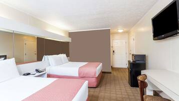 A hotel room with two beds, a desk, a television, and a small kitchenette.