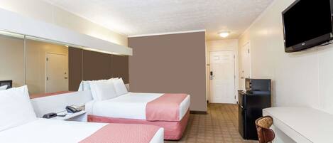 A hotel room with two beds, a desk, a television, and a small kitchenette.