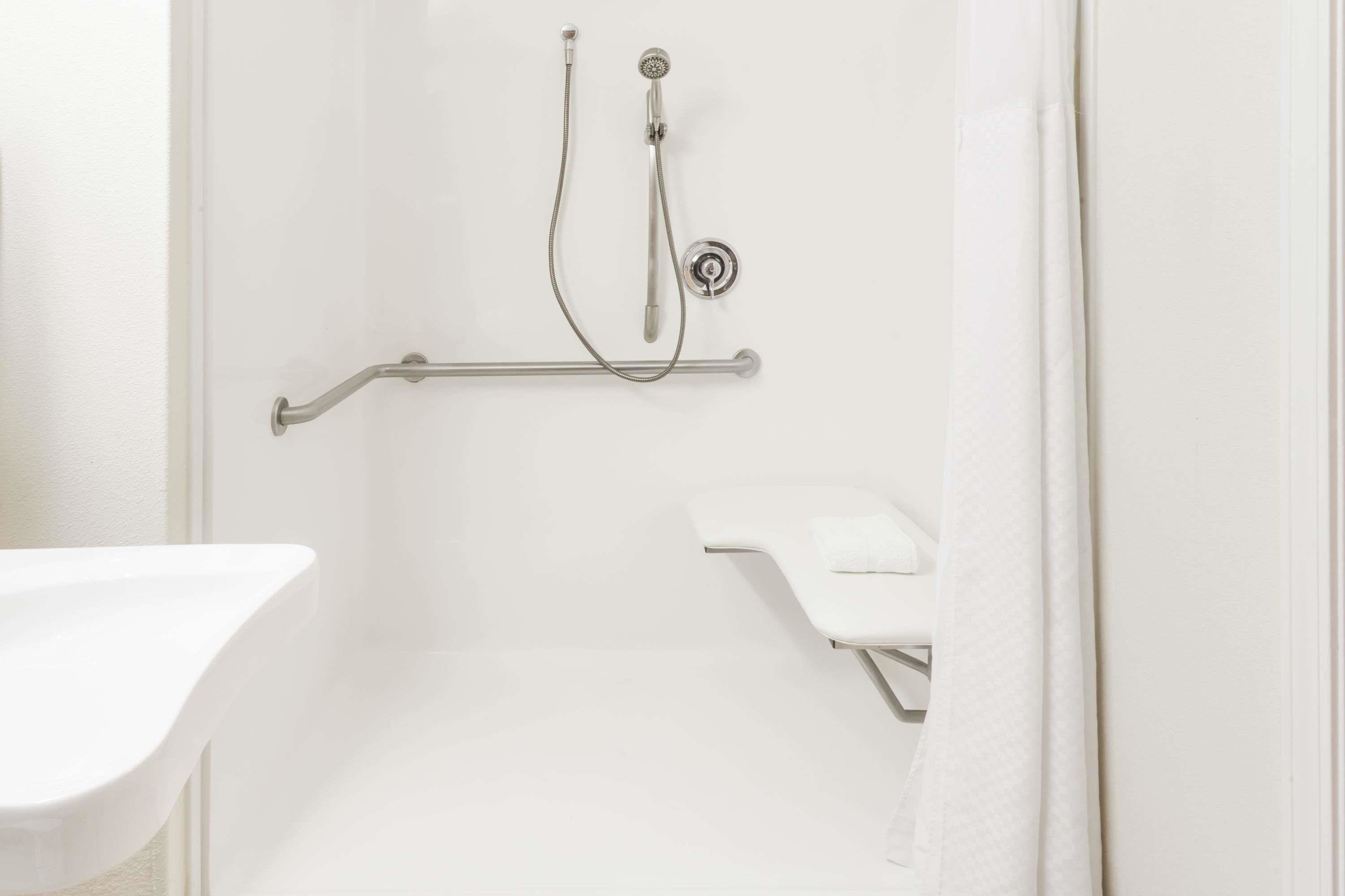 A bathroom with a shower, a grab bar, and a white sink.
