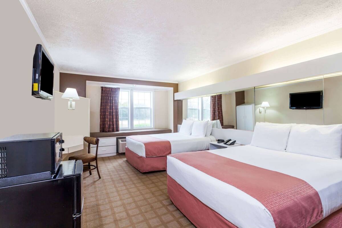 A hotel room with two beds, a desk, a chair, a TV, and a mirror.