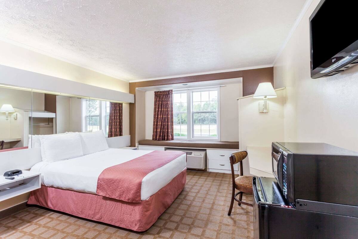 A hotel room with a bed, a desk, a chair, a TV, and a microwave.
