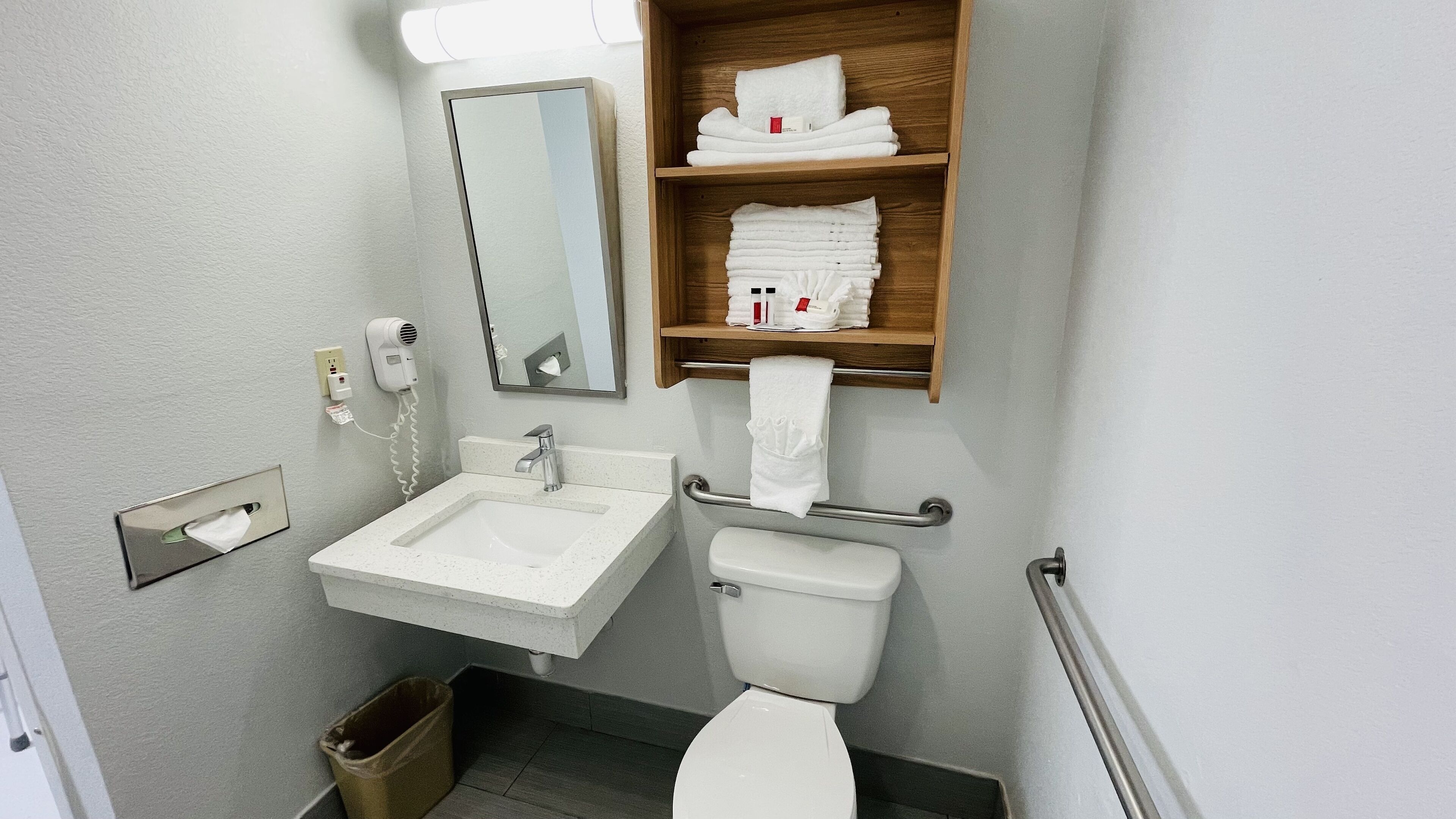 A bathroom with a sink, mirror, toilet, and a shelf with towels.
