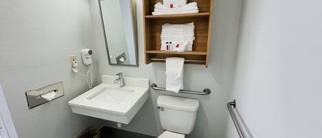 A bathroom with a sink, mirror, toilet, and a shelf with towels.