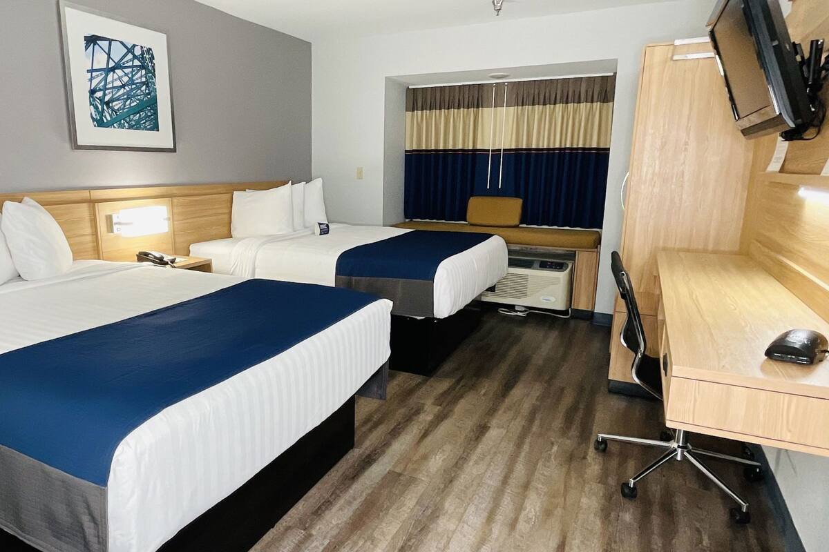 A hotel room with two beds, a desk, a chair, a TV, and a window with curtains.