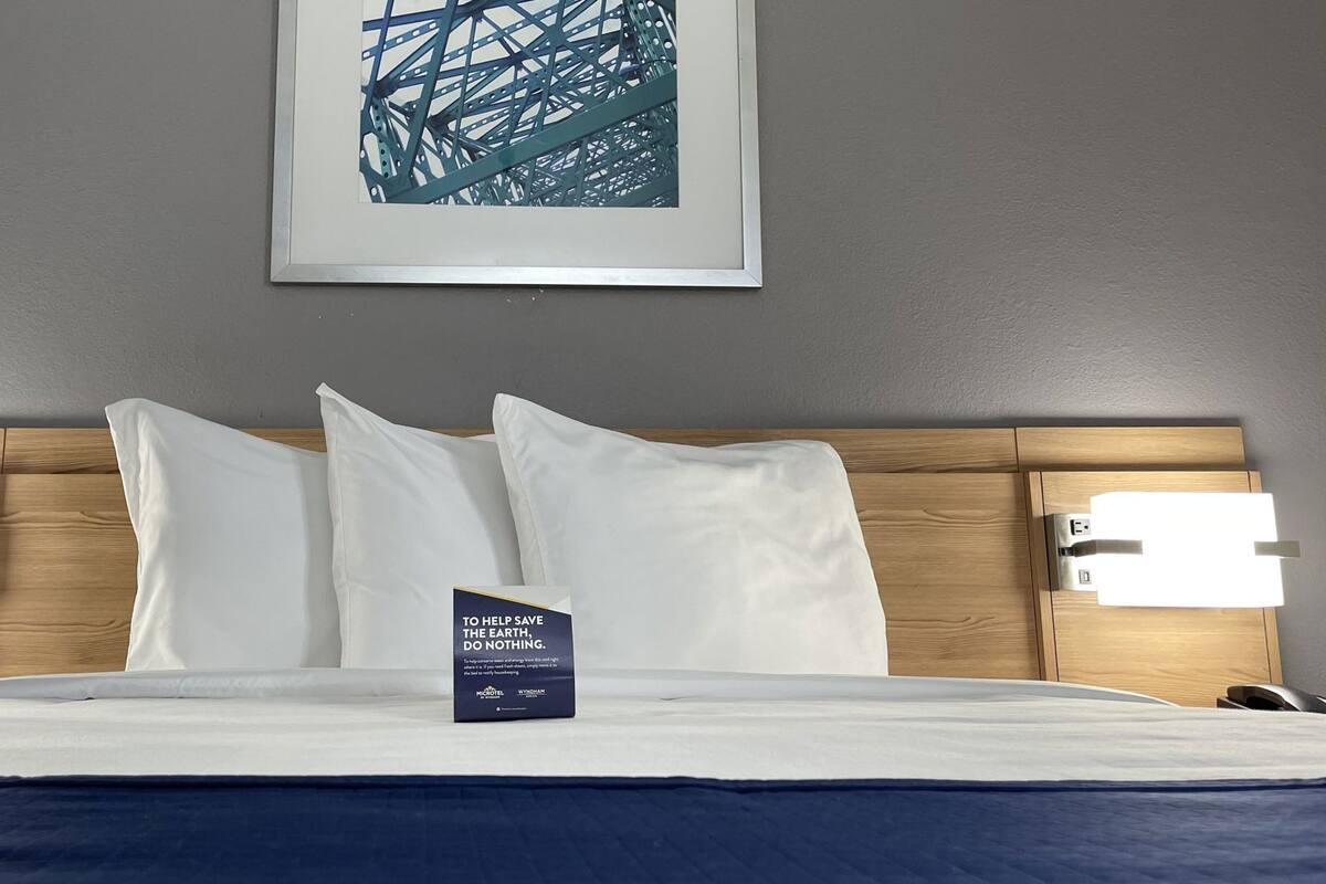 A neatly made bed with white linens, a framed picture above, and two wall-mounted light fixtures on either side.