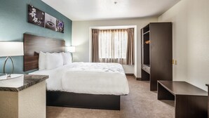A hotel room with a bed, a desk, a wardrobe, a window with curtains, and wall art. - Sleep Inn & Suites Tallahassee-Capitol (Tallahassee)