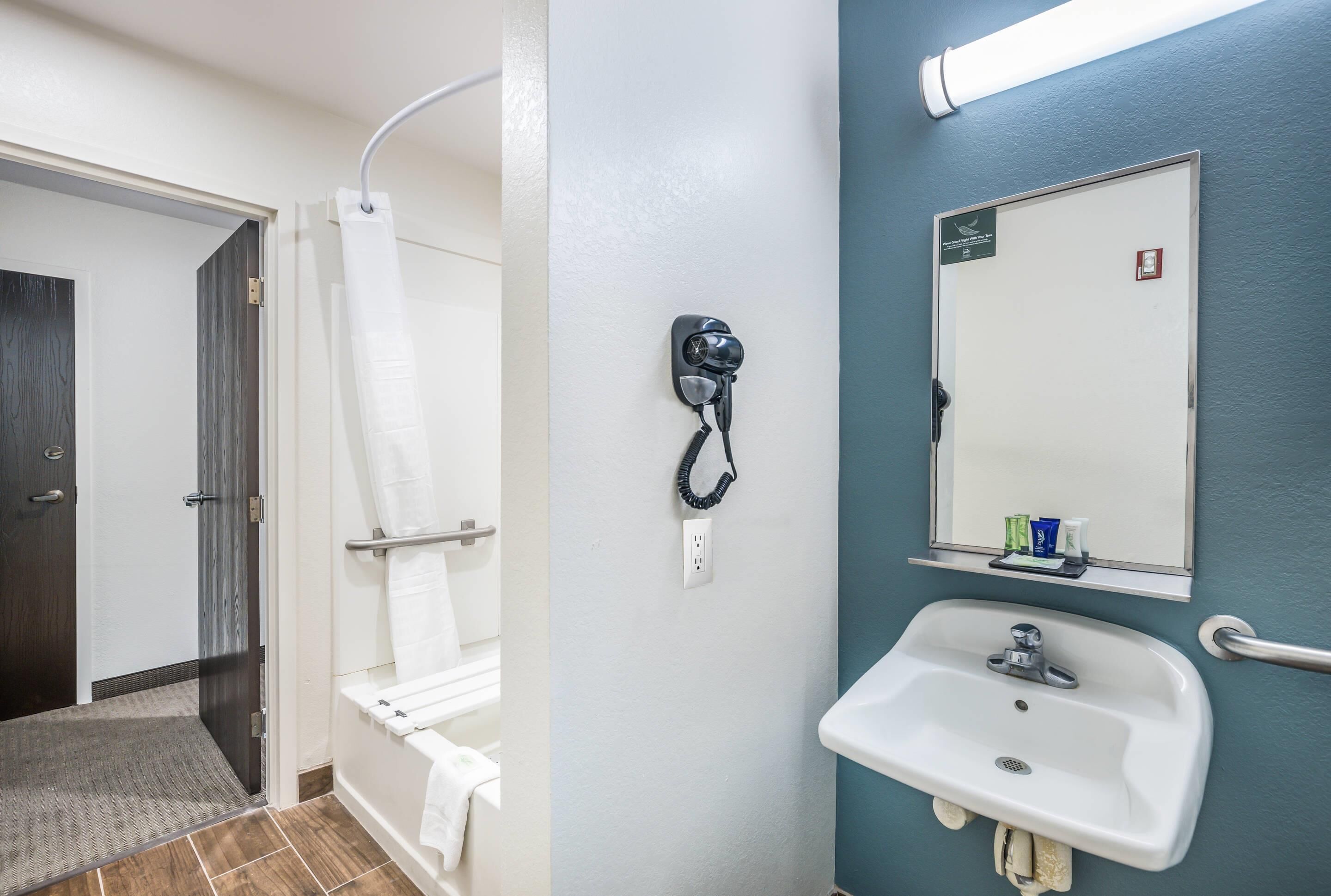 A bathroom with a shower, a hairdryer, a sink, and a mirror.