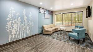 A room with a beige sofa, a blue armchair, a small table, and a large window with a view of trees. - Sleep Inn & Suites Tallahassee-Capitol (Tallahassee)