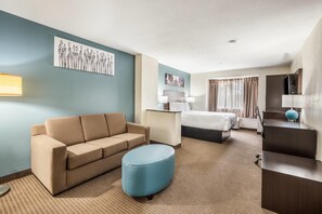 A hotel room with a sofa, ottoman, bed, desk, and artwork on the walls. - Sleep Inn & Suites Tallahassee-Capitol (Tallahassee)