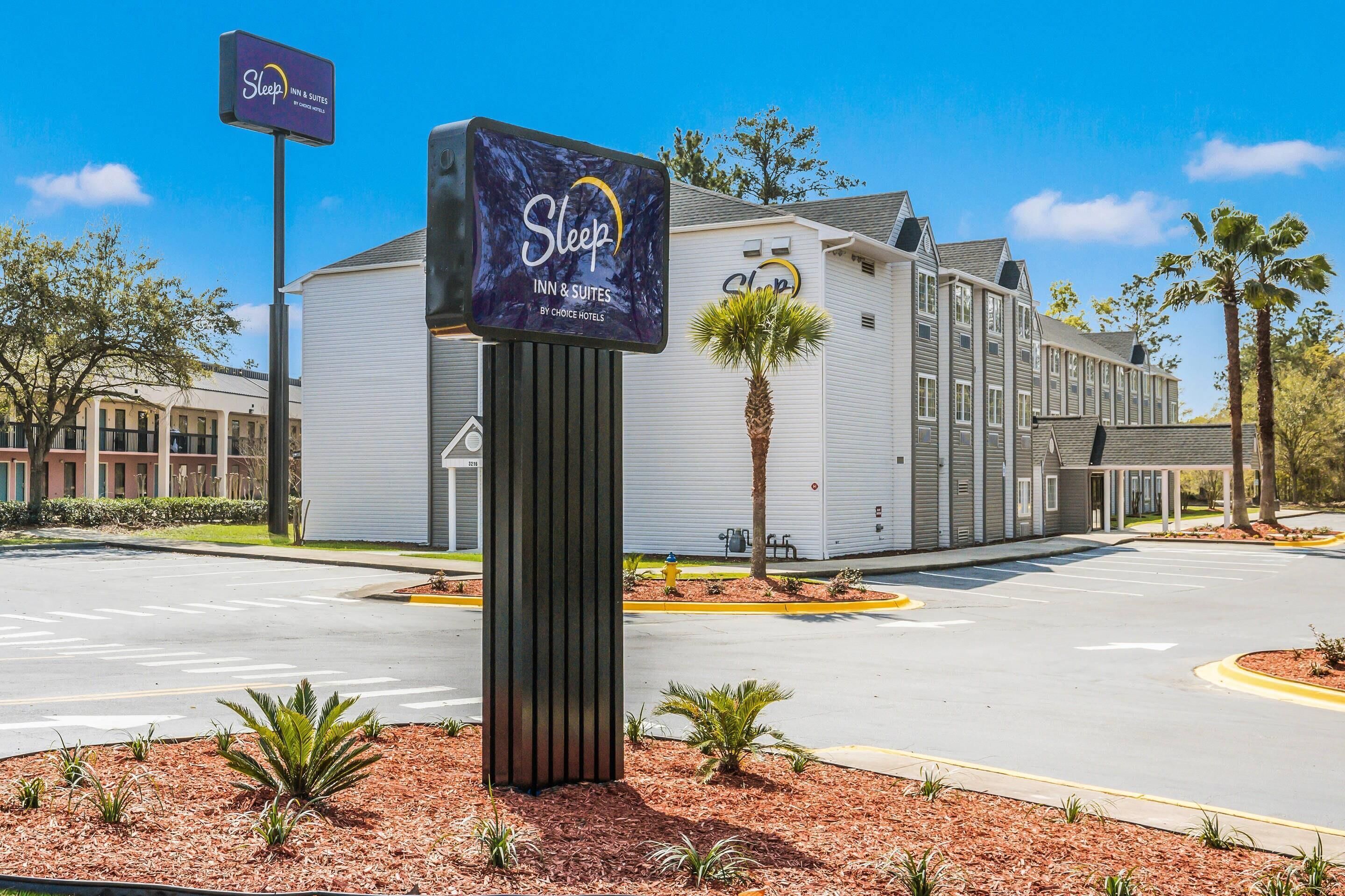 A Sleep Inn & Suites by Choice Hotels with a large sign, a parking lot, and a building with a modern design.