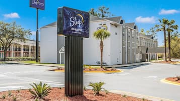 Een Sleep Inn & Suites by Choice Hotels met een groot bord, een parkeerplaats en een gebouw met een modern ontwerp.
