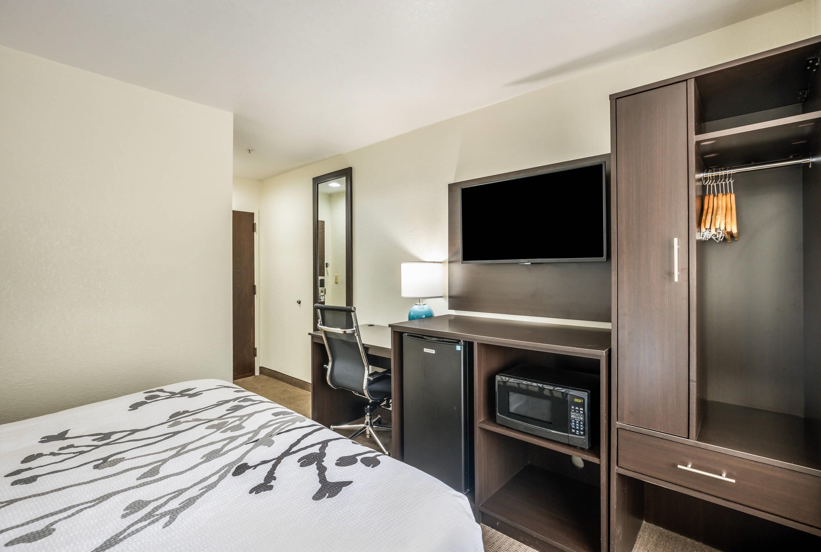 A hotel room with a bed, a desk with a computer, a television, a microwave, and a wardrobe.