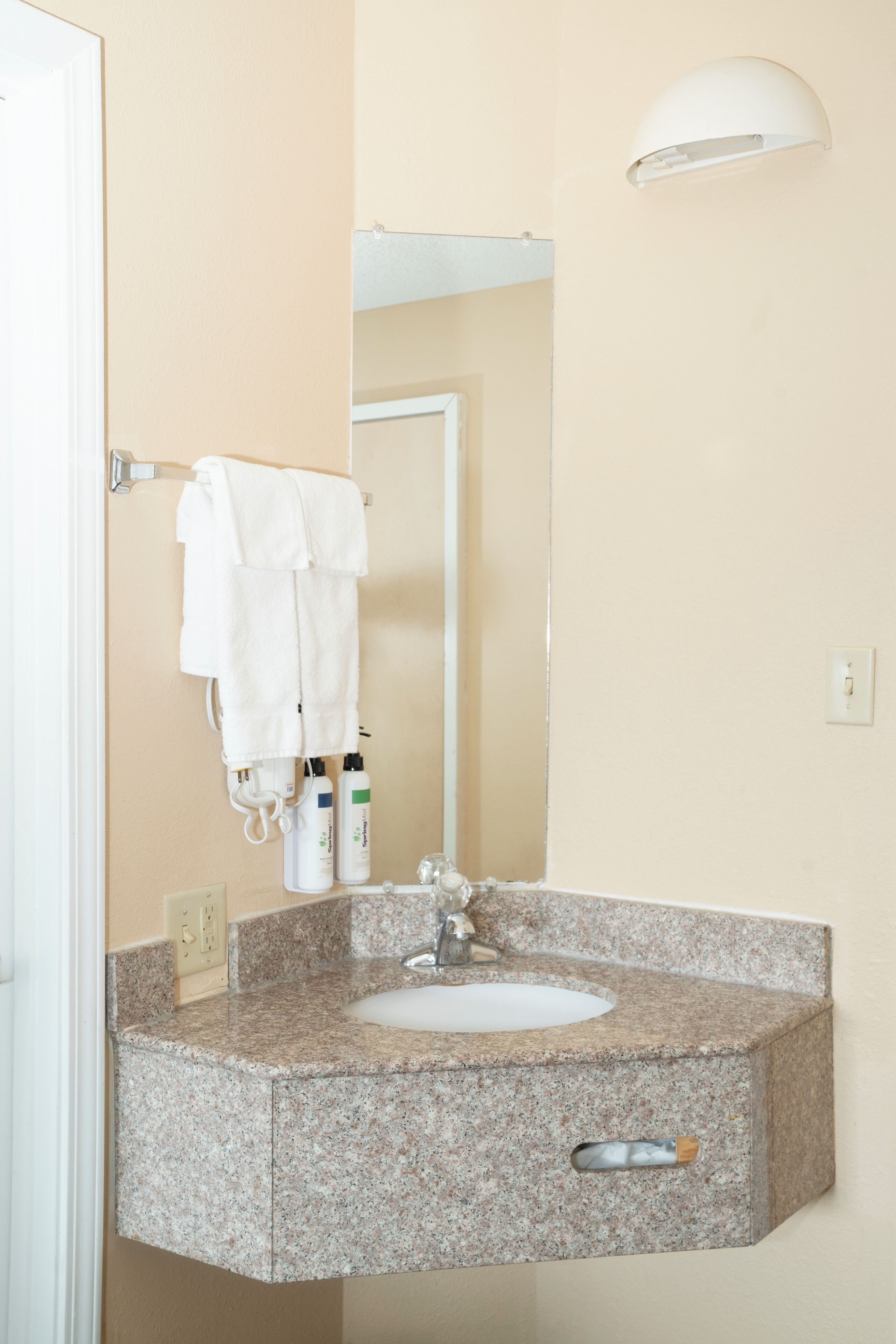 A bathroom with a granite sink, a mirror, and a towel rack with two towels.