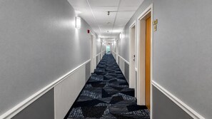 A hotel hallway with a carpeted floor, white walls, and doors on both sides. - Guest Inn Pigeon Forge (Pigeon Forge)