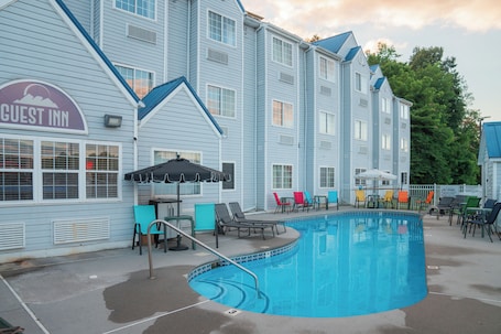 A pool area with lounge chairs and umbrellas, a sign for the Guest Inn, and a building with multiple windows and a blue roof.