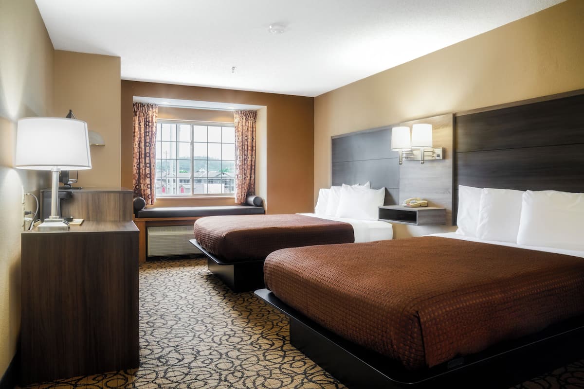 A hotel room with two beds, a desk, a lamp, a window with curtains, and a headboard with lights.