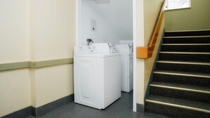 A laundry area with two white washing machines, a wooden staircase, and a door leading to another room.