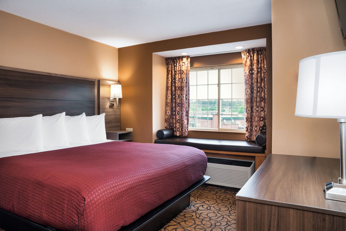A hotel room with a large bed, a desk with a lamp, a window with curtains, and a view of the outside.