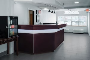 A reception area with a counter, a refrigerator, and a window with blinds.