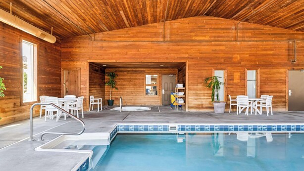 An indoor swimming pool with wooden walls and a covered ceiling, surrounded by white chairs and tables. - Comfort Inn Worland Hwy 16 to Yellowstone (Worland)